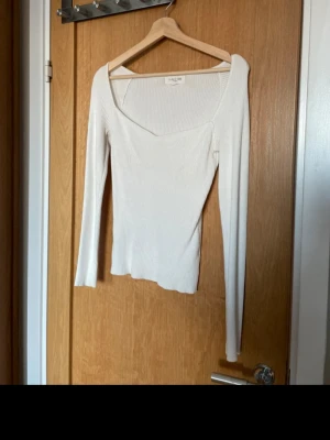 Vit ribbad topp från Astrid Frank - Trendig vit ribbad topp från Astrid Frank  med lång ärm och snygg, asymmetrisk halsringning. Toppen är croppad och har en figurnära passform.