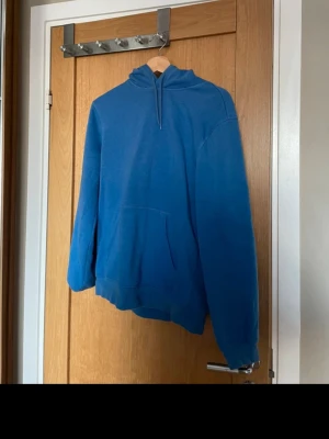 Blå hoodie från H&M Relaxed Fit - Snygg blå hoodie från H&M i relaxed fit. Hoodien har huva med dragsko och en stor magficka framtill. Tillverkad i mjukt material som känns skönt mot huden. Perfekt för en chill och avslappnad stil.