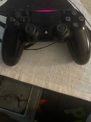 Svart PlayStation 4 DualShock handkontroll - En svart PlayStation 4 DualShock handkontroll med klassisk layout, två analoga spakar, styrkors och färgade symbolknappar. Tillverkad i plast med en matt finish och touchpad i mitten. Perfekt för gaming på PS4.