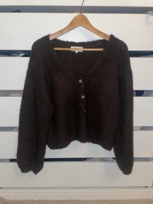 Brun kofta från Gina Tricot XS - Mysig brun kofta från Gina Tricot i ullmix med v-ringning och tre knappar framtill. Koftan har lång ärm och en lite fluffig, stickad känsla som passar perfekt till lager på lager. Enkel och stilren design som är lätt att matcha.