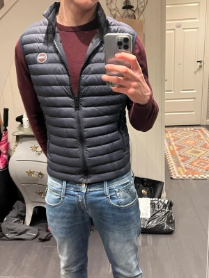 Mörkblå dunväst från Colmar - Snygg mörkblå dunväst från Colmar med quiltad design och hög krage. Västen har två dragkedjeförsedda fickor och ett tydligt Colmar-märke på bröstet. Perfekt att slänga över en hoodie eller tröja för extra värme och stil🤩. Skick 9/10🙌. Tveka inte att ställa frågor🤝