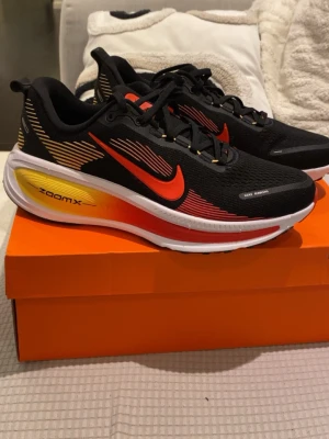 Nike ZoomX svart/röd/gul sneakers - Snygga Nike ZoomX sneakers i svart med röda och gula detaljer. Skorna har en ventilerande mesh-överdel, klassisk Nike Swoosh i rött och en färgskiftande sula med ZoomX-dämpning för extra komfort. Perfekta för dig som vill ha både stil och funktion. Pris går att diskutera
