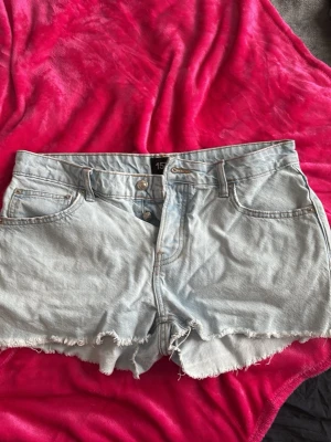 Ljusblå jeansshorts från 157 - Ljusblå jeansshorts från 157 med rå kant och knappgylf. Storlekslappen är borta men är i stl L!  Klassisk femficksmodell i bomull med hög midja och avslappnad passform. Perfekta för varma dagar och enkel att matcha med olika toppar. Har använt dem men ser nya ut! Säljer pågrund av de är för stora och aldrig kommer till användning!