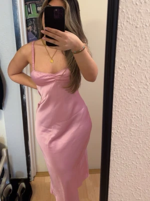 Rosa långklänning med smala axelband från Zara - Säljer en söt rosa långklänning med smala axelband och figurnära passform. Klänningen har en enkel, stilren design och är gjord i ett glansigt material. 