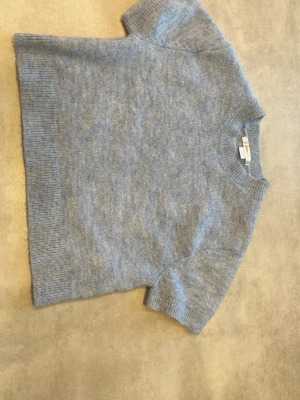 Ljusblå stickad tröja Gina Tricot - Mysig ljusblå stickad tröja från Gina Tricot med korta ärmar och ribbade detaljer vid hals, ärmslut och nederkant. Perfekt för lager på lager och enkel att matcha med jeans eller kjol. 