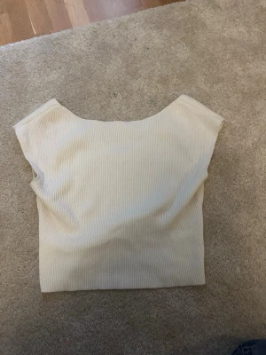Ribbad beige croppad topp - Säljer en ribbad croppad topp i beige med v-ringning framtill. Toppen är ärmlös och har en enkel, stilren design som passar perfekt till jeans eller kjol. Materialet känns mjukt och stretchigt för en bekväm passform. Är i storlek 168-164 men skulle säga snäppet större skulle den passa. Säljer då den är för stor för mig 