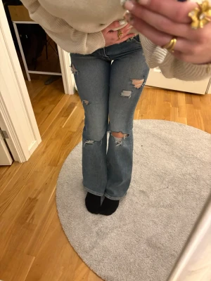Blå slitna bootcut jeans - Säljer ett par blå bootcut jeans med flera slitningar och hål på benen som är självgjorda. 💓