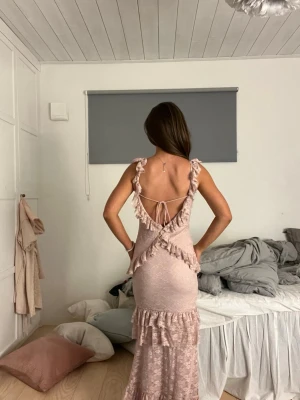 Ljusrosa balklänning med volanger - Romantisk långklänning i ljusrosa spets med volangdetaljer och öppen rygg med snörning. Klänninhen är uppsydd och passar min som är 168, den går hela vägen till marken. 