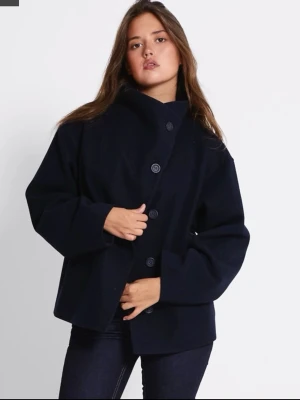 Blå kappa (LÅNAD BILD FRÅN HEMSIDAN)  - Blå kappa med unik asymmetrisk knäppning framtill. Jackan har en hög krage, stora knappar och en loose passform. Köptes för 400 kr men pris går att diskutera. 