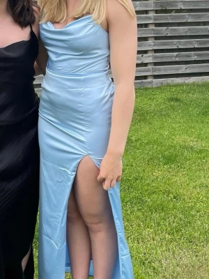 Ljusblå satin långklänning med slits - Ljusblå ”satin” klänning med slit från Nelly Klänningen går ner till fötterna på mig som är 170cm Endast använd vid ett tillfälle så nästan som ny! Skulle säga att den passar storlekar 36 också då axelbanden osv är stretchiga