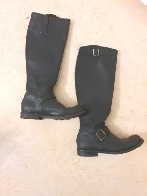 Primeboots, Stövlar, Svart, EUR 37 - Ett par svarta stövlar med dragkedja bak och spänne på sidan. Enkel "flärp" på insidan som man använder för att ta på sig stövlarna enklare samt stänga dem. Dessa är en av Primeboots bästa modeller. Rekommenderar att köpa ny innersula.  Se bilder för egen bedömning.