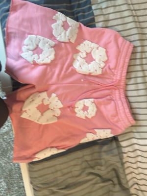 Rosa shorts med vita blommor - Unika rosa shorts med stora vita blommor i ett puffigt tyg. Shortsen har resår i midjan för skön passform och är perfekta för dig som vill sticka ut. Materialet känns mjukt och bekvämt, och designen är riktigt trendig.
