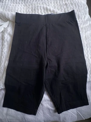 Svarta cykelshorts från Divided - Svarta cykelshorts från Divided H&M med hög midja och stretchigt material. Perfekta för en sportig look eller att bära under kjol eller klänning. Klassisk och enkel design utan synliga detaljer.