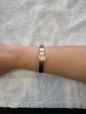 Guldigt armband med stor kristall - Snyggt armband i metall med guldfärgad finish och en stor, rund klar kristall i mitten från lenmer. Armbandet har en stilren och modern design med blanka ytor och en cirkelformad detalj runt stenen. Perfekt för dig som gillar statement-smycken. Armbandet har några defekter därav priset! Armbandet är 18cm i omkrets! OBS: FRAKTAR INOM 24H!🩷