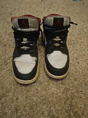 Air Jordan 1 Retro High OG svart/vit/röd - Säljer ett par klassiska Air Jordan 1 Retro High OG sneakers i svart, vitt och rött läder. Skorna har den ikoniska röda swoosh-loggan på sidan, svart snörning och högt skaft. Perfekta för dig som gillar streetwear och vill ha en tidlös sneaker med retrovibbar.