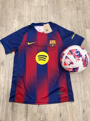 FC Barcelona matchtröja Nike - Snygg FC Barcelona matchtröja från Nike i klassiska blå och röda ränder. Tröjan har klubbmärke, Nike-logga och Spotify som sponsor framtill samt UNHCR-logga bak. Tillverkad i lätt och ventilerande polyester, perfekt för fotboll eller träning.