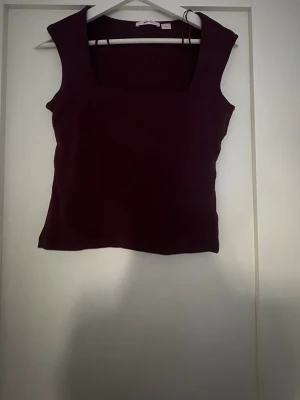 Vinröd ärmlös topp från Gina Tricot - Snygg vinröd topp från Gina Tricot med fyrkantig ringning och ärmlös design. Perfekt att styla med jeans eller kjol för en trendig look. Materialet känns mjukt och stretchigt, vilket gör den bekväm att bära hela dagen.