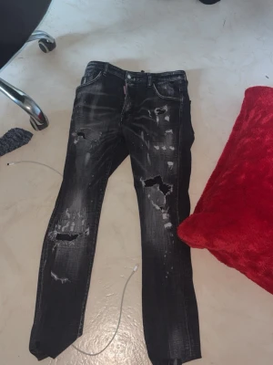 Svarta slitna jeans från Dsquared2 - Säljer ett par svarta distressed jeans från Dsquared2 med flera slitningar och hål för en edgy look. Jeansen har en smal passform, klassisk femficksmodell och tydliga tvätteffekter. Perfekta för dig som gillar streetstyle och vill sticka ut.