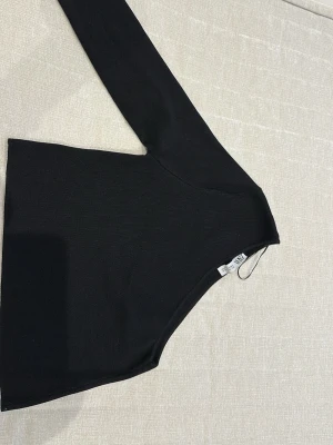 Svart oneshoulder topp från Zara - Trendig svart oneshoulder topp från Zara med lång ärm på ena sidan och axelbandslös på andra. Tunn, stretchig kvalitet som sitter snyggt och passar perfekt till höga jeans eller kjol. Enkel men stilren design som känns modern.
