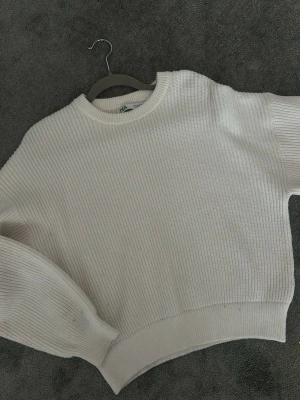 Vit ribbstickad tröja från Zara - Säljer en vit ribbstickad tröja från Zara med rund halsringning och breda muddar. Tröjan har en avslappnad passform och långa ärmar, perfekt för lager på lager. Materialet är mjukt och stretchigt för extra komfort.