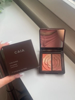 CAIA Sun Filter Duo Palette Golden Tan - Snygg bronzer duo från CAIA i nyansen Golden Tan. Paletten innehåller två skimrande puder i varma, gyllene toner och kommer i en stilren brun kompakt med spegel. Perfekt för att skapa en solkysst look med glow. Den är helt oöppnad som man ser eftersom det är tejp kvar, den som jag visar på bilden är en annan som jag själv använder. Fick en när jag fyllde år och jag hade precis köpt en då.