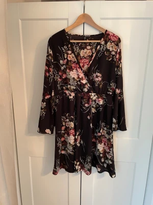 Blommig blus/klänning  - Supersöt kort klänning från Shein med svart botten och blommigt mönster i rosa, beige och grönt. Klänningen har v-ringning, långa ärmar och ett flowy fall. Perfekt för dig som gillar romantiska vibes och vill sticka ut lite extra.längd: 96 cm