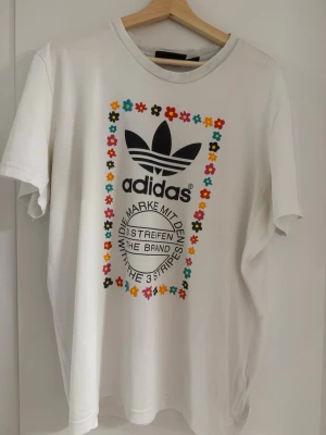 adidas Originals x Pharrell Williams Flower Trefoil T-shirt XL - Säljer en adidas Originals x Pharrell Williams Flower Trefoil T-shirt i vit. Storlek XL.
