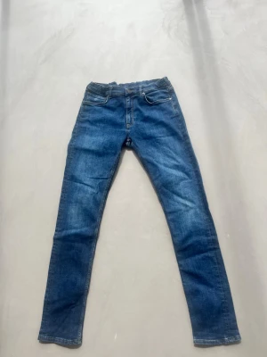 Blå skinny jeans med fyra fickor - Säljer ett par klassiska blå skinny jeans med fem fickor och normal midja. Jeansen har en snygg tvätt med lätt slitning och raka ben. Perfekta till vardagslooken och passar till det mesta. Stängs med dragkedja och knapp.