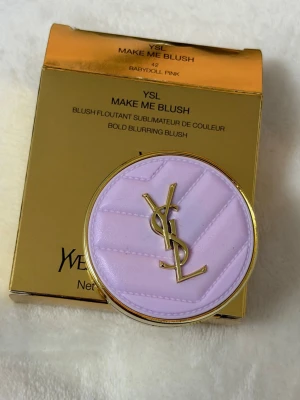 YSL Make Me Blush Babydoll Pink - Lyxigt rouge från Yves Saint Laurent i nyansen Babydoll Pink. Kommer i en rund, guldig dosa med ljust lila lock och YSL-logga i metall. Rouget har en silkeslen, pressad formula och ger en fräsch rosa ton till kinderna.