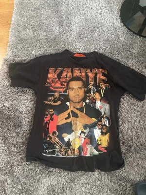 Svart Kanye West t-shirt med tryck - Använd PostNord när ni beställer.                          Cool svart t-shirt med stort färgglatt tryck av Kanye West och olika motiv från hans karriär både fram och bak. T-shirten har klassisk passform och rund hals. Perfekt för dig som gillar streetwear och vill sticka ut med en unik design.
