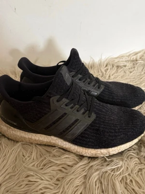 Adidas Ultra Boost - Svarta Adidas Ultra Boost sneakers med stickad ovandel och klassiska tre ränder i plast på sidorna. Skorna har en vit Boost-sula som ger extra komfort och respons. Perfekta för dig som gillar sportig stil och vill ha riktigt sköna sneakers.