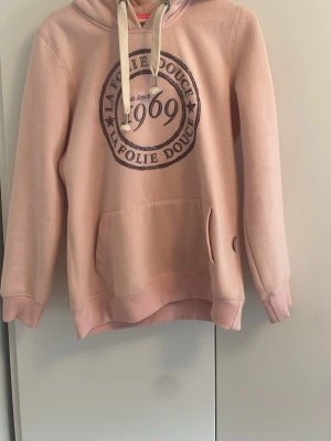 Rosa hoodie från La Folie Douce - Snygg ljusrosa hoodie från La Folie Douce med stor magficka, huva med vita snören och tryck framtill med texten '1969'. Mjuk borstad insida och ribbade muddar. Köpt i Valdi för ett par år sedan för 800spänn.