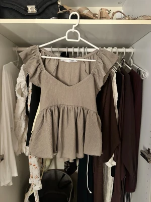 Beige volangblus med v-ringning - Supersöt beige blus med volanger på axlarna och v-ringad hals. Perfekt att styla med jeans eller kjol för en trendig look.