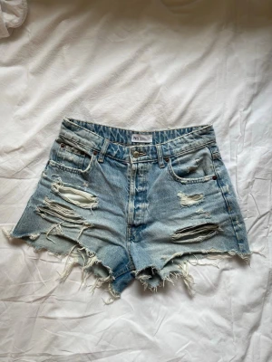 Ljusblå jeansshorts  - Super snygga ”slitna” ljusblå jeansshorts från Zara. I mycket bra skick! Midjemått 37 cm.