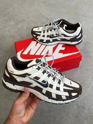 Nike P-6000 bruna och vita sneakers - Nike P-6000 sneakers i brunt och vitt med mesh och syntetiska överdrag. Skorna har en chunky sula, silverfärgade detaljer och klassisk Swoosh på sidan. Snygg retrostil med sportig vibe och lågt skaft. Perfekta för dig som gillar streetwear och komfort.