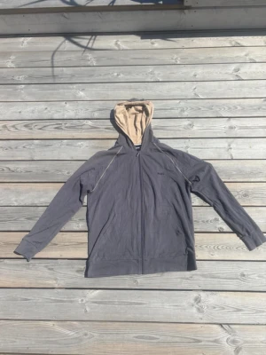 Grå hoodie med dragkedja från BOSS - Snygg grå hoodie från BOSS med dragkedja framtill och beige insida på huvan. Diskret BOSS-logga broderad på bröstet. Hoodien har långa ärmar, fickor på sidorna och är tillverkad i mjukt bomullsmaterial. Perfekt för en avslappnad och stilren look.