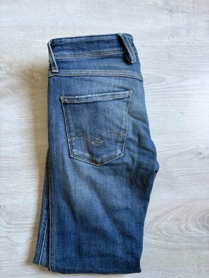 Blå slim fit jeans med slitningar - Snygga blå slim fit jeans med lätt slitna detaljer och klassisk femficksdesign. Jeansen har en något tvättad look och smala ben. Perfekta för en avslappnad och trendig stil. Materialet är troligtvis bomull med lite stretch för extra komfort.