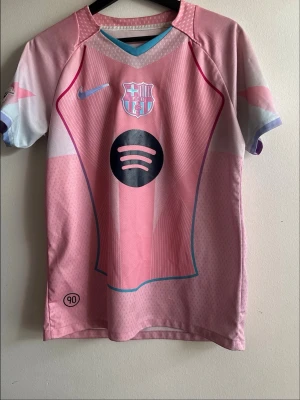 Rosa FC Barcelona matchtröja Raphinha - Säljer en rosa FC Barcelona matchtröja från Nike med Raphinha och nummer 11 på ryggen. Tröjan har klubbmärke och sponsorlogga framtill, samt blå detaljer och korta ärmar. Perfekt för dig som älskar fotboll och vill sticka ut på planen.