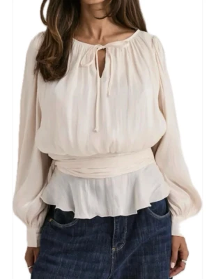 Krämvit blus med knyt och volang - Snygg krämvit blus med långa puffärmar, knytband vid halsen och volang nedtill. Tillverkad i ett lätt, luftigt tyg som ger en romantisk känsla. Perfekt att styla med jeans eller kjol för en trendig look. 🌸 Ny med prislapp kvar!