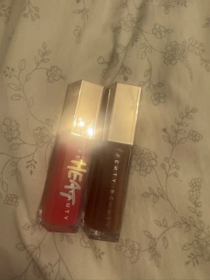 Fenty Beauty Gloss Bomb duo - Två läppglans från Fenty Beauty, Gloss Bomb-serien. Ena är i färgen Hot Cherry, en intensiv röd nyans, och den andra är en mörkare brun ton. Båda har glansig finish och kommer i snygga fyrkantiga förpackningar med silvriga lock. Har bara använt en gång båda två 