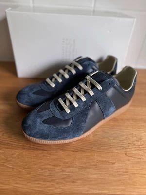 Maison Margiela Gats - Säljer ett par maison margiela gats navy. De köptes nyligen men har tyvärr bara blivit stående i garderoben och kommer helt enkelt inte till användning. De är i absolut toppskick, i princip som nya! Detaljer:  Skick: 9.5/10 – Använda ytterst få gånger, minimalt med spår av användning. Storlek: 44 Medföljer: Allt original; box, dustbag etc. Skickas snabbt, säkert och spårbart (oftast samma dag eller dagen efter köp).