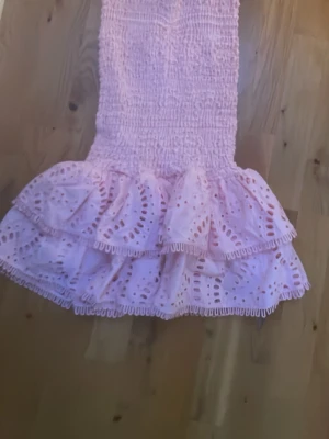 Ljusrosa klänning med volang och broderi - Supersöt klänning i ljusrosa med dubbla volanger och broderade detaljer. Klänningen  har smock i midjan för skön passform och är gjord i ett lätt bomullstyg. Perfekt för sommarens alla tillfällen! Pris kan diskuteras‼️