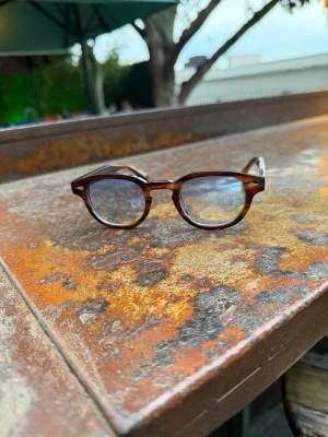 Solglasögon med blått glas  - Säljer ett par bruna solglasögon med rund form och klassisk retrostil. Bågarna är i plast med en skön brun ton och glasen är lätt tonade. Perfekta för dig som vill ha en tidlös accessoar med vintagekänsla.