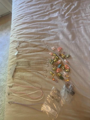 Mixade halsband med färgglada hängen - Säljer ett gäng halsband i olika stilar och färger. Här finns tunna guldfärgade kedjor och band i rosa, vitt och lila. Hängena är lekfulla och föreställer bland annat avokado, regnbågar, blommor och söta figurer. Perfekt för dig som gillar att mixa och matcha accessoarer