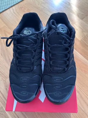 Svarta Nike Air Max Plus  - Helsvarta Nike Air Max Plus skor i stl. 45 med klassisk vågig design och Air-dämpning i sulan. Perfekta för dig som gillar streetwear och sportig stil. Inköpta från Nikes officiella hemsida för 2399 kr (kvitto finns). Sonen har endast använt dom en gång, alltså är skorna i nyskick. 
