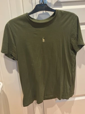 Ralph lauren t-shirt Olivgrön - Snygg olivgrön t-shirt i bomull med klassisk rund hals och korta ärmar. På bröstet finns en liten broderad logga i beige som ger en stilren touch. Perfekt basplagg till alla outfits. M passar S