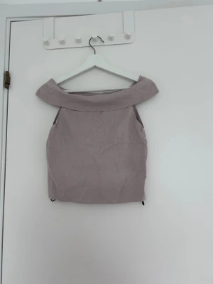 Beige offshoulder topp - Trendig beige offshoulder topp med bred krage och ärmlös design. Toppen har en mjuk, ribbad struktur och är perfekt för dig som vill ha en stilren och modern look. Passar snyggt till både jeans och kjol.