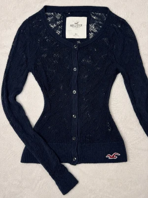 Marinblå vintage Hollister spetskofta  - Skitsnygg marinblå kofta från Hollister i spetsstickat ihåligt material. Toppen sitter fint på och är väldigt eftertraktad och sällsynt! (Finns ett litet hål men de smälter in i mönstret så de syns inte alls!) 💕Har ännu fler Hollister toppar uppe på mitt konto så kolla in dem!