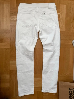 Vita raka jeans från Lee - Säljer ett par vita jeans från Lee med rak passform och klassisk femficksdesign. Jeansen har bälteshällor, knappgylf och Lee-logga på bakfickan. Perfekta för dig som vill ha en clean och stilren look. 🔥 Jag säljer dom de var lite för stora för mig. Köpta för cirka en månad sen och andvändts ett fåtal gånger.