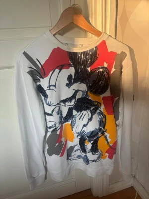 Vit sweatshirt med Mickey Mouse från Iceberg - Säljer en vit sweatshirt från Iceberg med en stor, färgstark Mickey Mouse-print i svart, rött, gult och grått på framsidan.  Iceberg är ett italienskt premiumvarumärke som är känt för sina Disney-samarbeten. Nypris ca 3500kr